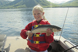 young girl smiles while holding up her salmon catch