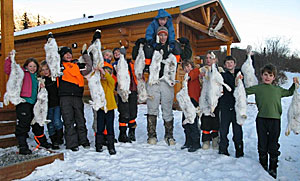 Group of kids outside a lodge holding up hares